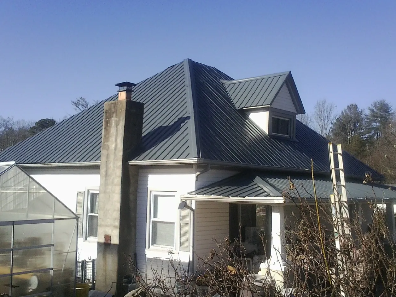 Dark blue standing seam metal roof on a white farmhouse with dormer — Slate & Tile Roof Repair by Roofing Brothers in Pineola
