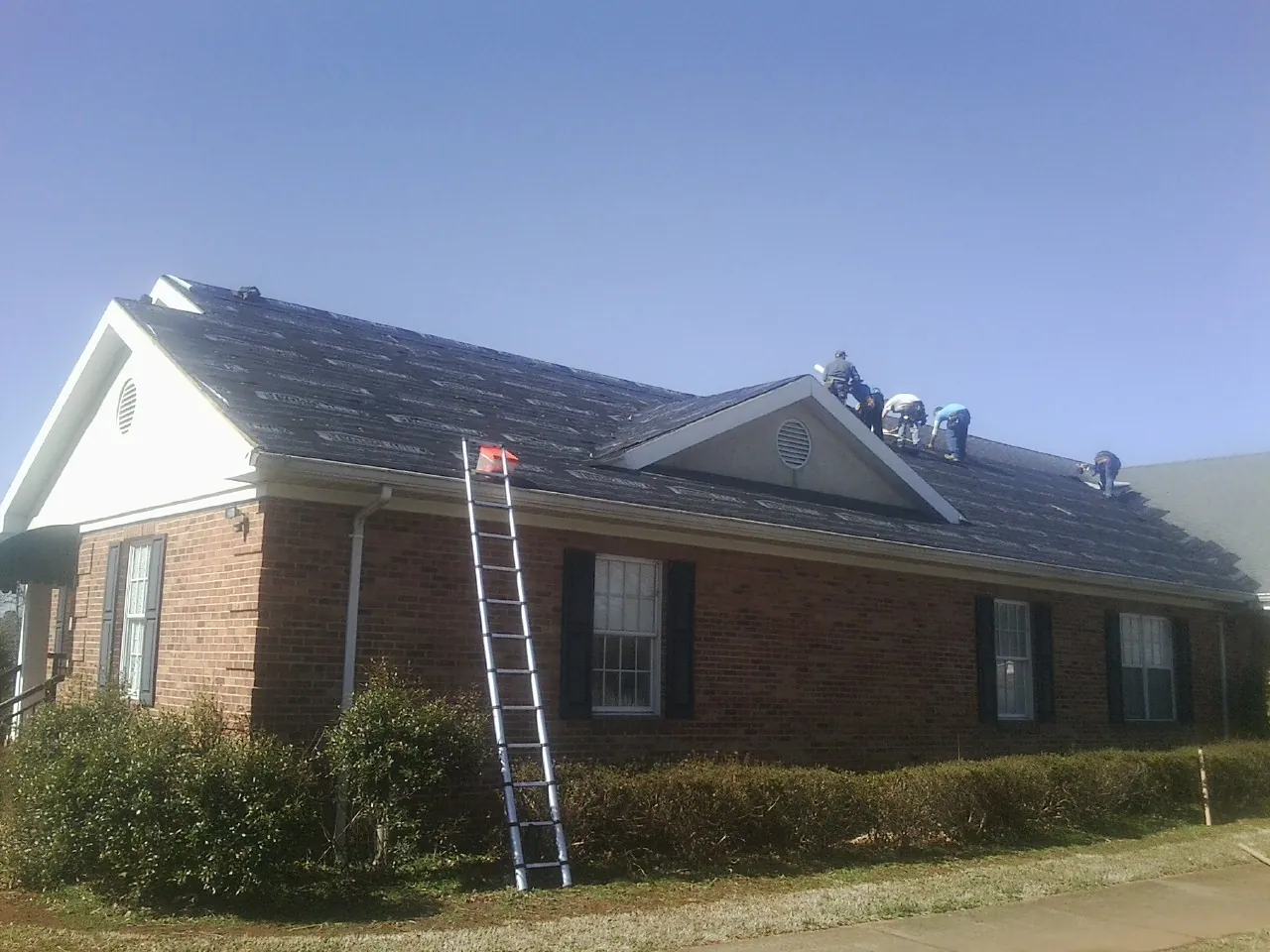 Crew tearing shingles off a brick ranch roof with a ladder set — Metal Roof Repair work by our crew in Pineola