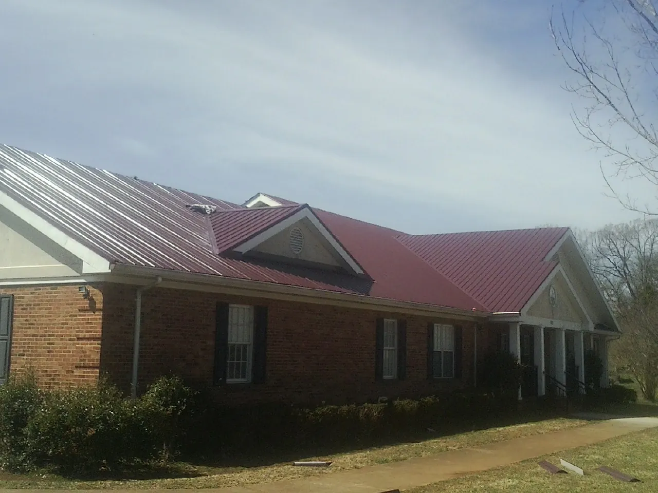 Red metal roof with gabled entries on a long brick building, from a Hail Damage Roof Repair job in Pineola