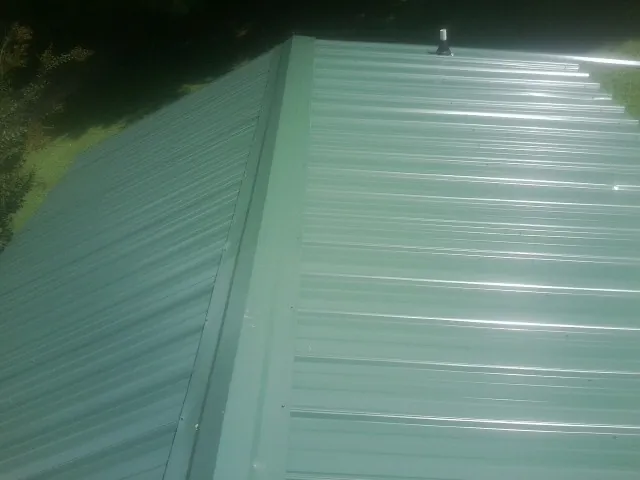 New green metal panels meeting at the ridge of a roof — Flat Roof Repair work by our crew in Pineola