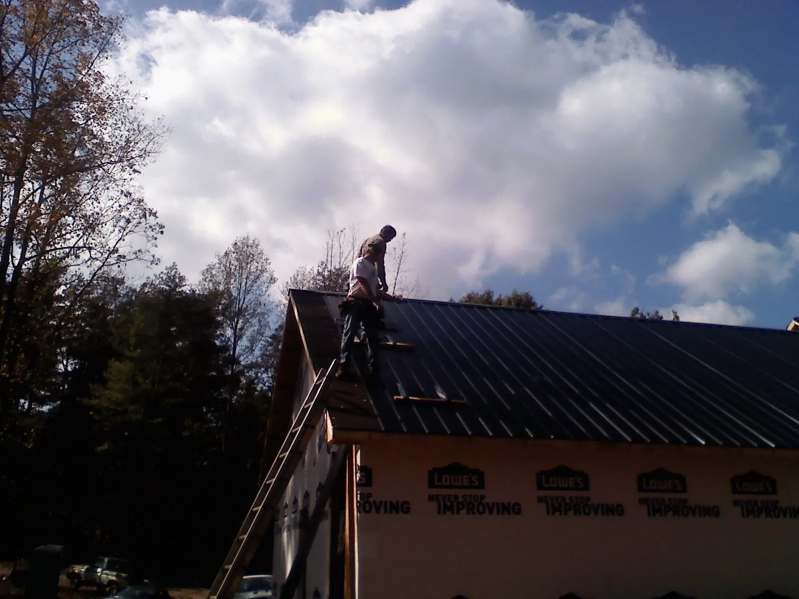 Roofer fastening dark metal panels high against a cloudy sky, from a Roof Inspection job in Pineola