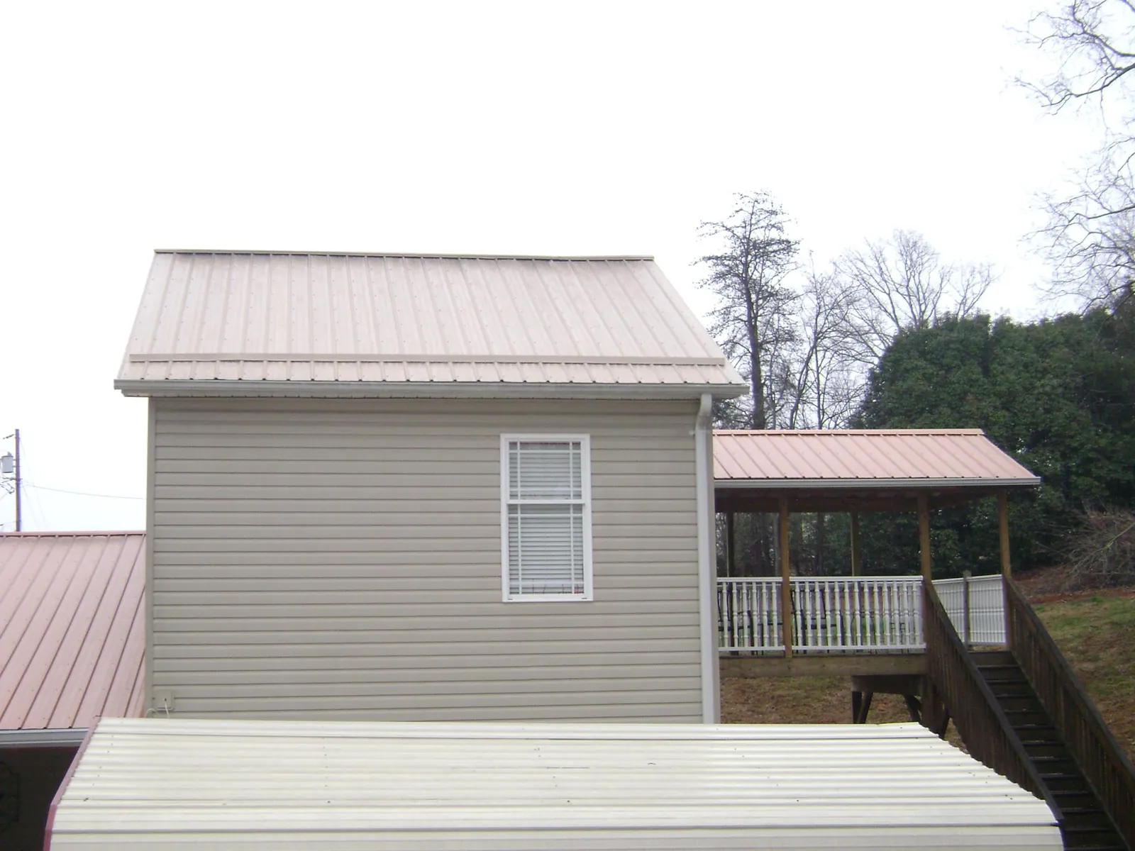 Tan metal roofs on a two story addition and attached porch, from a Roof Replacement job in Pineola